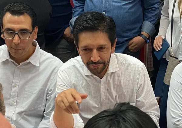 Foto colorida de homem branco com cabelo preto e camisa branca, sentado, olhando para o lado - Metrópoles