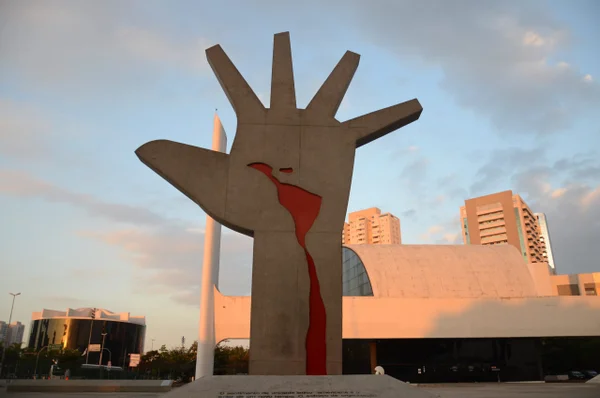 imagem colorida mostra escultura em forma de mão, com desenho vermelho no meio presentando a américa latina