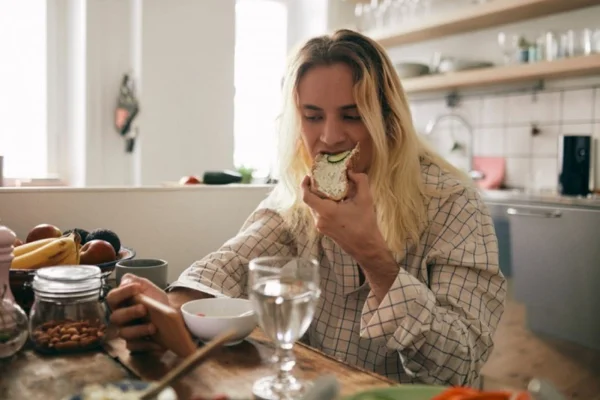 Uma mulher se alimento e assintindo vídeo no celular ao mesmo tempo