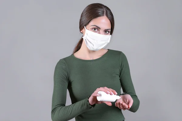 Mulher usando máscara branca e passando álcool em gel- Metrópoles