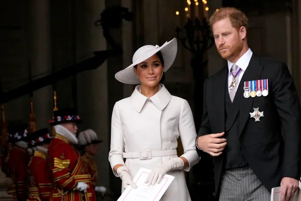 Foto colorida. Mulher negra usa um vestido e um chapéu branco. Ao seu lado, está um homem branco, de cabelos ruivos. Ele está vestindo um terno preto com algumas medalhas de honra e uma camisa branca