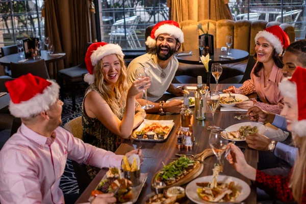 Imagem colorida: seis pessoas sentadas ao redor da mesa em uma confraternização de Natal