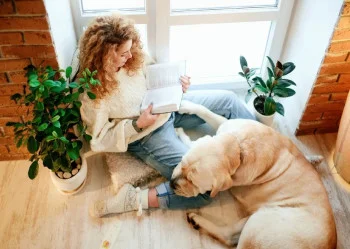 mulher negra lendo livro sentada no chão ao lado de um cachorro grande