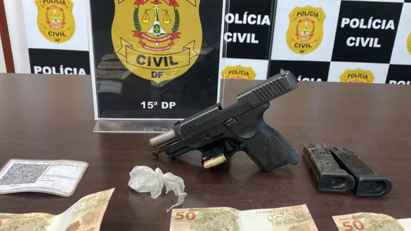 Foto colorida de arma de fogo e porção de cocaína em cima de mesa de apreensão da polícia civil