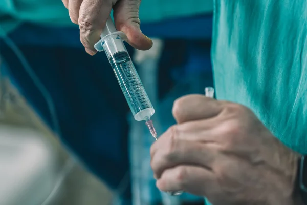 Close-up da mão do anestesista masculino com uma seringa e frasco nas mãos na sala de cirurgia. Metrópoles