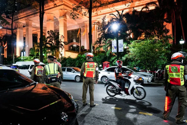 Imagem colorida de fachada de hotel cercado por policiais tailandeses - Metrópoles