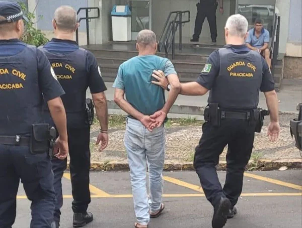 Imagem de agentes da Guarda Municipal conduzindo homem de camiseta azul à delegacia - Metrópoles