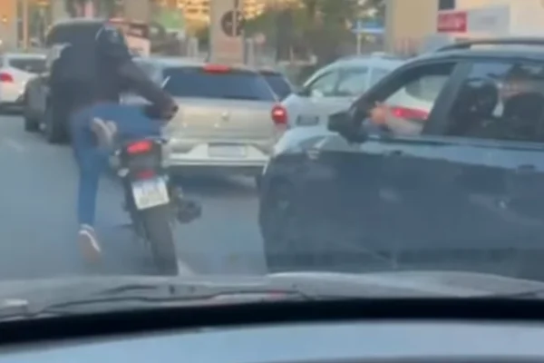 Imagem colorida do ladrão de moto ao lado do carro parado no trânsito enquanto o motorista aponta a arma pela janela. Metrópoles