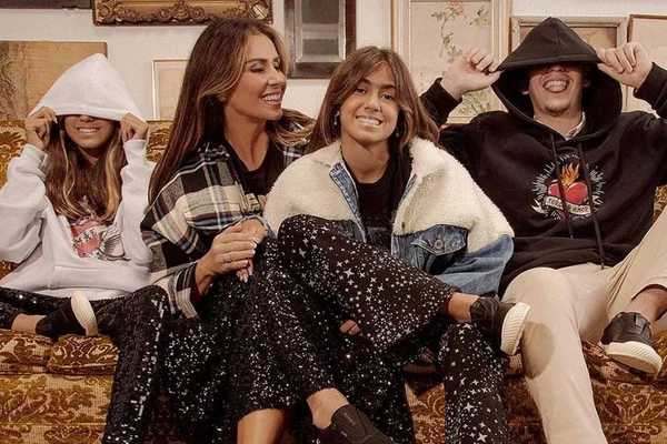 A atriz Giovanna Antonelli sentada no sofá com seus três filhos, um garoto mais velho e duas meninas gêmeas. Eles usam roupas da marca Reserva.