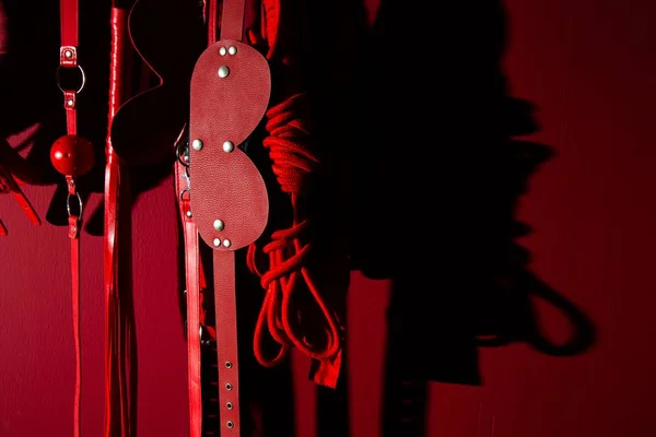 Itens BDSM dispostos em uma parede vermelha - Metrópoles