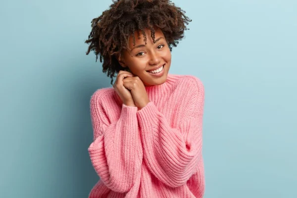 Mulher negra de blusa rosa com as mãos no rosto e sorrindo - Metrópoles