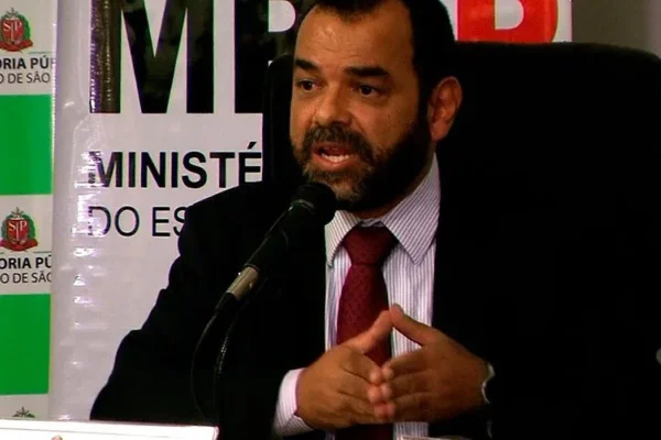 Homem negro fala enquanto está sentado à frente de um banner do Ministério Público de São Paulo
