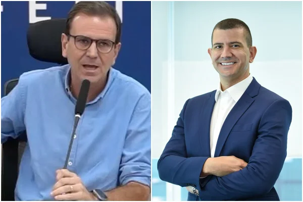 Eduardo Paes está de camisa social azul e fala em um microfone e Douglas Ruas está de terno e braços cruzados