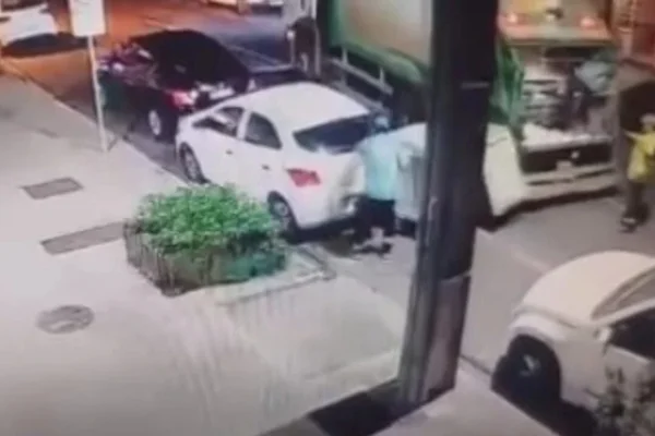 Foto colorida de momento que conteiner de lixo atinge carro estacionado durante coleta no Paraná