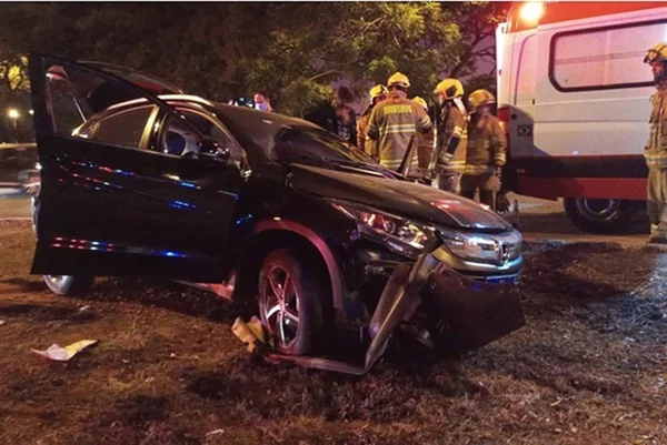 Carro preto amassado em grama e bombeiros ao lado, junto de viatura