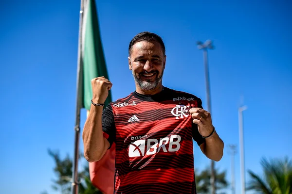 Novo técnico do Flamengo, Vítor Pereira, sorri, ergue o punho em riste e segura logo do time na camisa em foto - Metrópoles