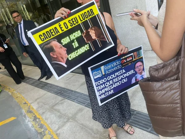 Imagem colorida mostra uma mulher segurando dois cartazes de protesto contra o ex-presidente Jair Bolsonaro em frente a um hospital - Metrópoles