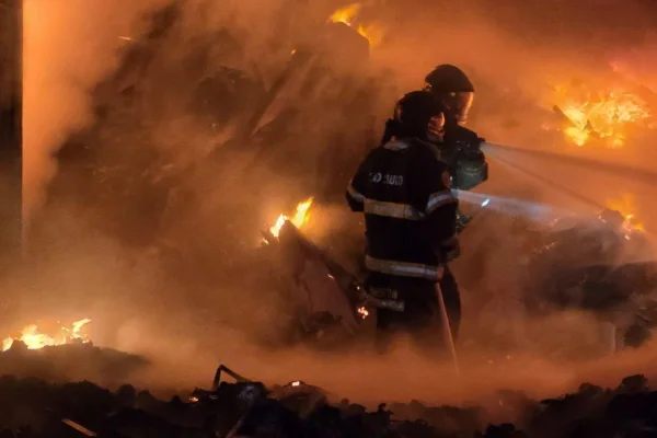 Imagem colorida mostra névoa envolvendo homens com roupas de bombeiros em meio a chamas de um incêndio - Metrópoles