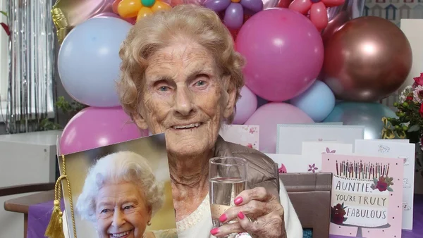 Mulher idosa segurando taça de bebida com balões de aniversário atrás