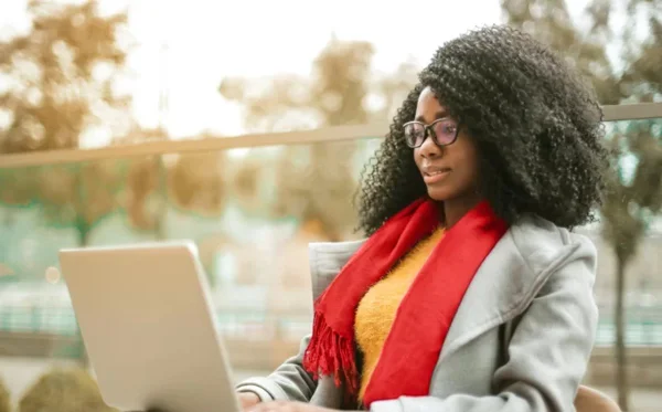 mulher negra e com os cabelos cheios e crespos trabalha ao ar livre com um computador