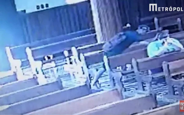 Foto: Homem de camisa preta e boné pegando uma bolsa de outra pessoa em uma igreja.