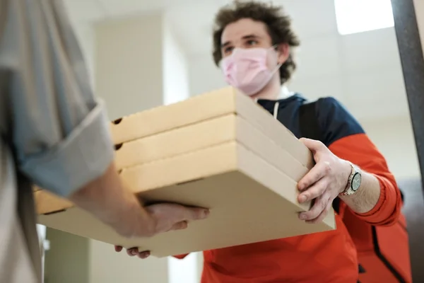 Entregador de pizza, usando máscara, entrega pizza a cliente