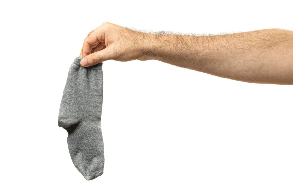 Mão segurando meias sujas isoladas. Lavanderia, conceito de tarefas domésticas, meia fedorenta, roupa íntima de algodão suada, meias sujas usadas em fundo branco. Metrópoles
