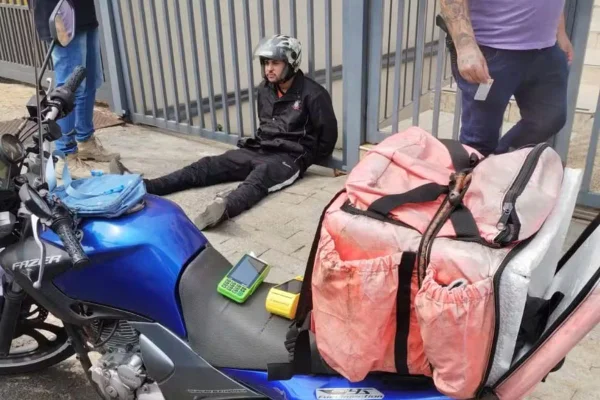 Imagem colorida mostra motoboy algemado no chão - Metrópoles