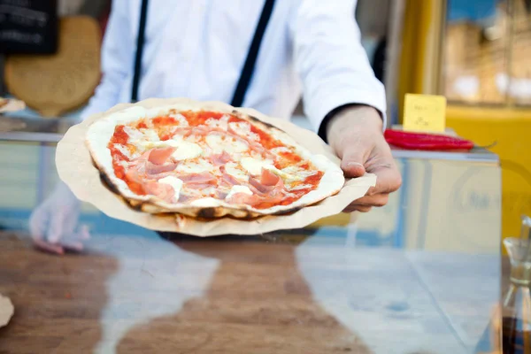 Foto colorida de um homem entregando uma pizza - Metrópoloes