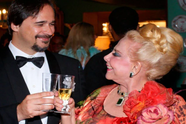 Homem branco com taça sorrindo para mulher branca com joias