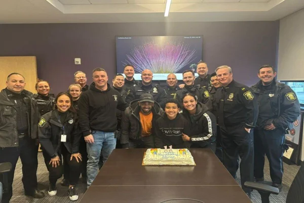 Imagem colorida de garoto rodeado por policiais, com bolo em cima de uma mesa - Metrópoles
