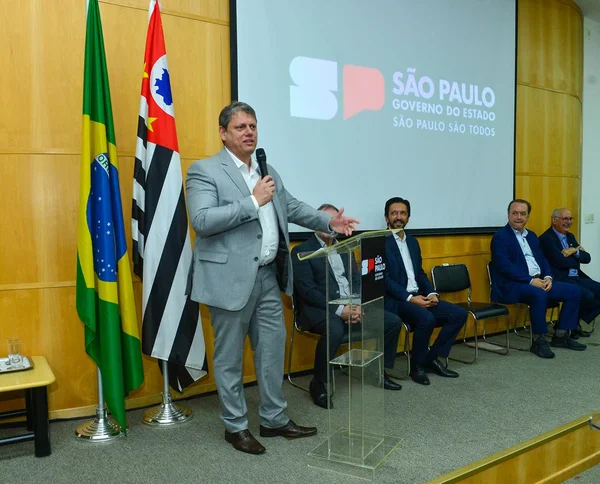 Imagem colorida mostra Tarcísio de Freitas, homem branco, grisalho, de terno cinza e camisa branca, falando em um microfone em um palco - Metrópoles