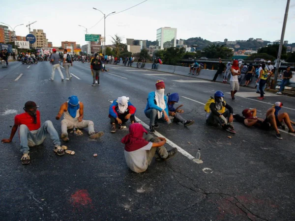 Manifestantes com os rostos cobertos sentam-se em rua de Caracas - Metrópoles