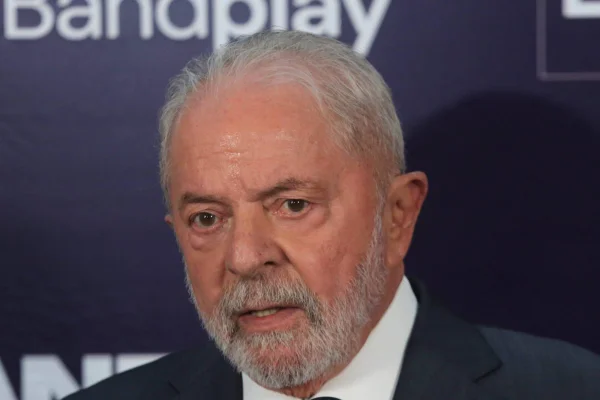 O candidato e ex-presidente Lula dá entrevista antes do debate da Bandeirantes. Ele olha para frente, usando terno, frente a um banner azul escuro - Metrópoles