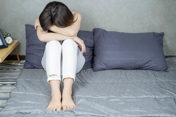 Mulher chora segurando joelhos, sentado em cama - Metrópoles