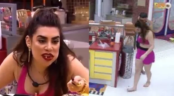 Na imagem colorida, uma mulher está posicionada no centro. Ela tem cabelos curtos e loiros, olhos castanhos e está com comida na boca enquanto fala