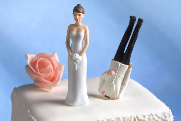 noivinhos em um bolo de casamento branco com o funDo azul. O noivo está com a cara enfiada no bolo.