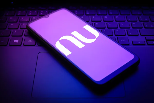 Imagem de telefone celular, em cima de um teclado de notebook, exibindo a logomarca do Nubank - Metrópoles