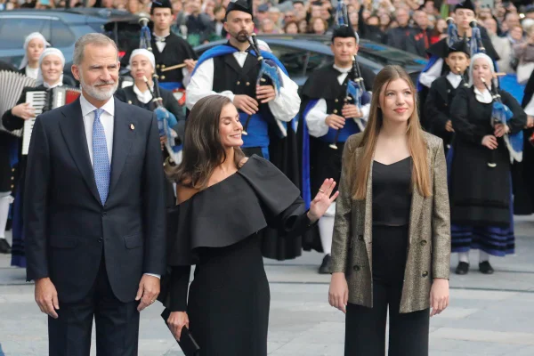 Foto colorida de homem de terno, mulher com vestido preto e mulher com blazer posando para foto. Eles estão rodeados por pessoas - Metrópoles