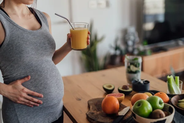 Foto colorida de mulher grávida com mão na barriga tomando suco - Metrópoles