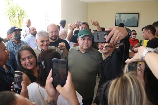 Governador do DF Ibaneis Rocha fala ao microfone para autoridades e lideranças locais. Ele traja boné e camisa verde escuro