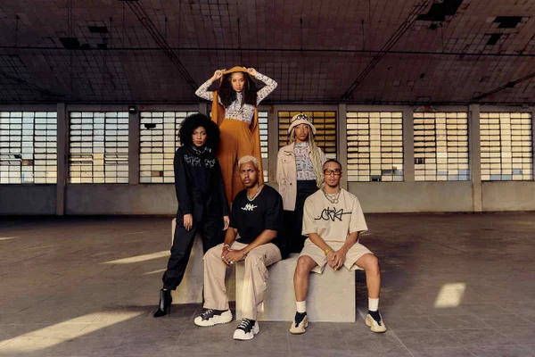Na imagem com cor, 5 pessoas em um banco branco posando para uma foto editorial da Riachuelo - Metrópoles