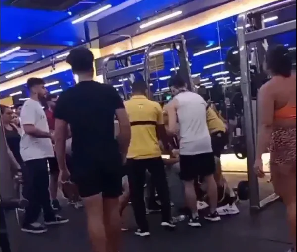 Imagem colorida de parte interna de academia com pessoas em volta de dois homens, que se agridem - Metrópoles