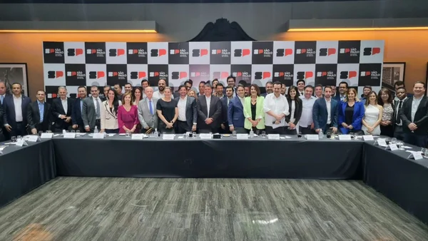 Imagem colorida mostra grupo de 50 pessoas, todas brancas e com roupas sociais, atrás de uma mesa de reuniões - Metrópoles