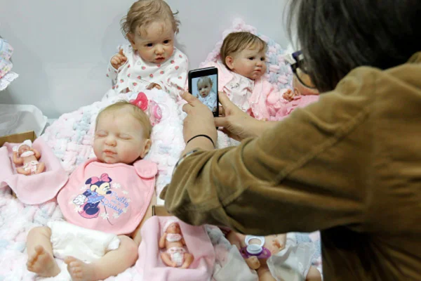 Imagem colorida de mulher tirando fotos de bonecas reborn