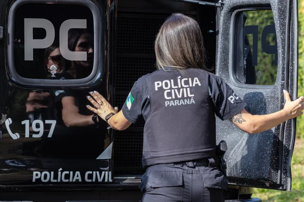 Foto colorida de uma agente da Polícia Civil fechando a porta da viatura - Metrópoles