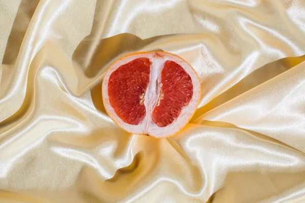 Toranja fresca em fundo de tecido de seda macio bege. Conceito de sexo. Saúde da mulher, sexualidade, tensão erótica. Símbolo feminino da vagina e do clitóris.