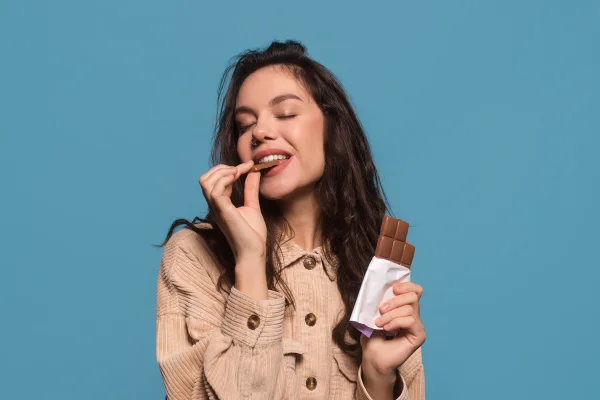 Foto colorida de mulher comendo chocolate - Metrópoles