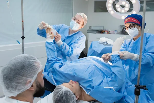 Foto mostra mãe na sala de parto tendo luvas colocadas por médicas