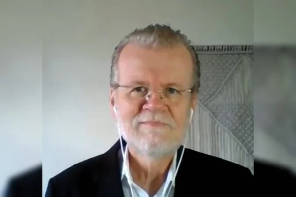 Homem branco de óculos veste camisa social branca e blazer escuro